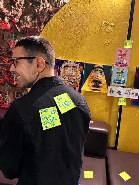 Dario di spalle davanti alle sue stampe, con due post-it sulla giacca: «lui è Dario» e «per info chiedete a lui».